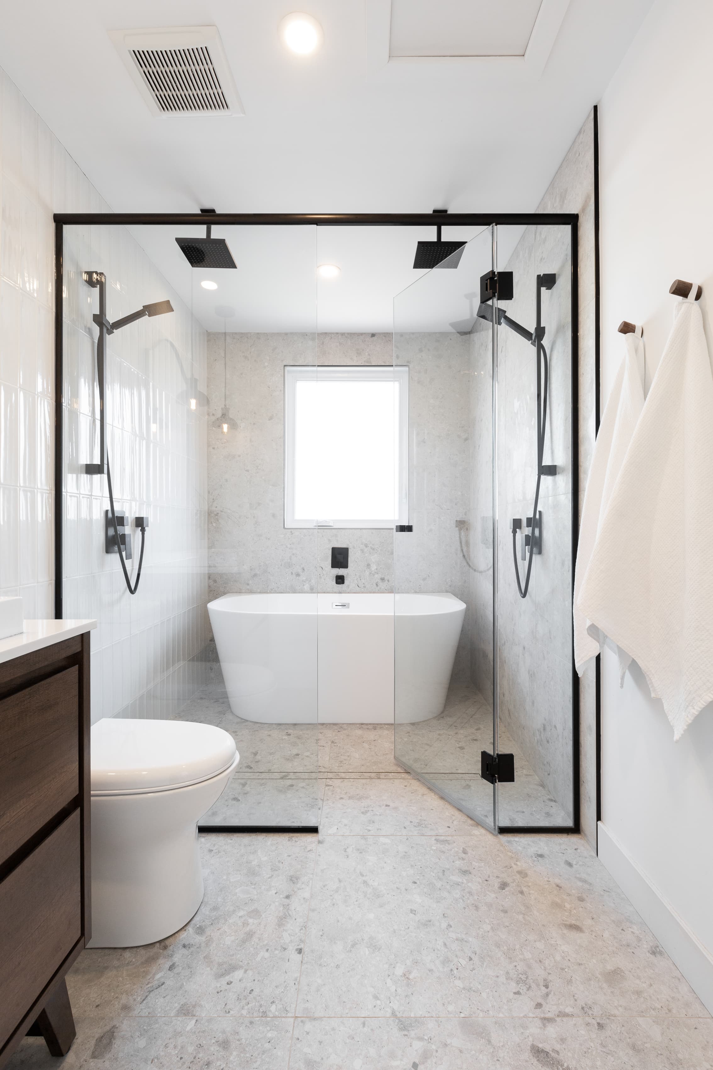Salle de bain moderne avec douche vitrée, baignoire îlot, robinetterie noire et carrelage gris clair.