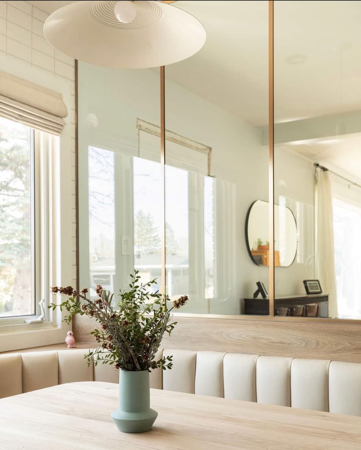 Coin repas moderne avec banquette crème, table en bois clair et grands miroirs muraux.