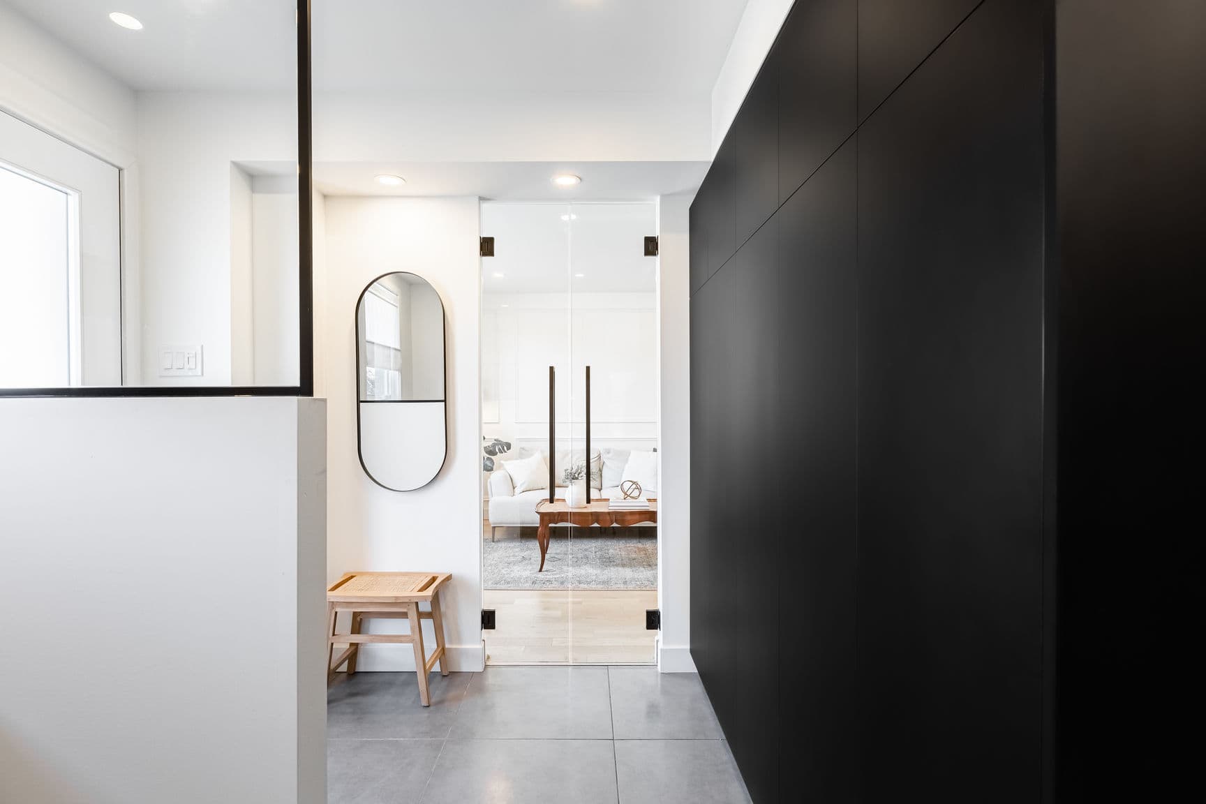 Entrée moderne avec mur noir mat, miroir ovale et portes vitrées menant au salon.